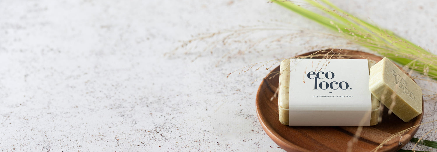 Savon artisanal avec le logo Eco Loco sur l'étiquette dans un bol en bois avec une branche et un fond blanc texturé comme une pierre de quartz