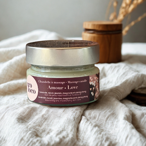Chandelle à massage Eco Loco Amour, soin nourrissant et hydratant, posée sur une couverture et devant un bouquet de fleurs séchées.