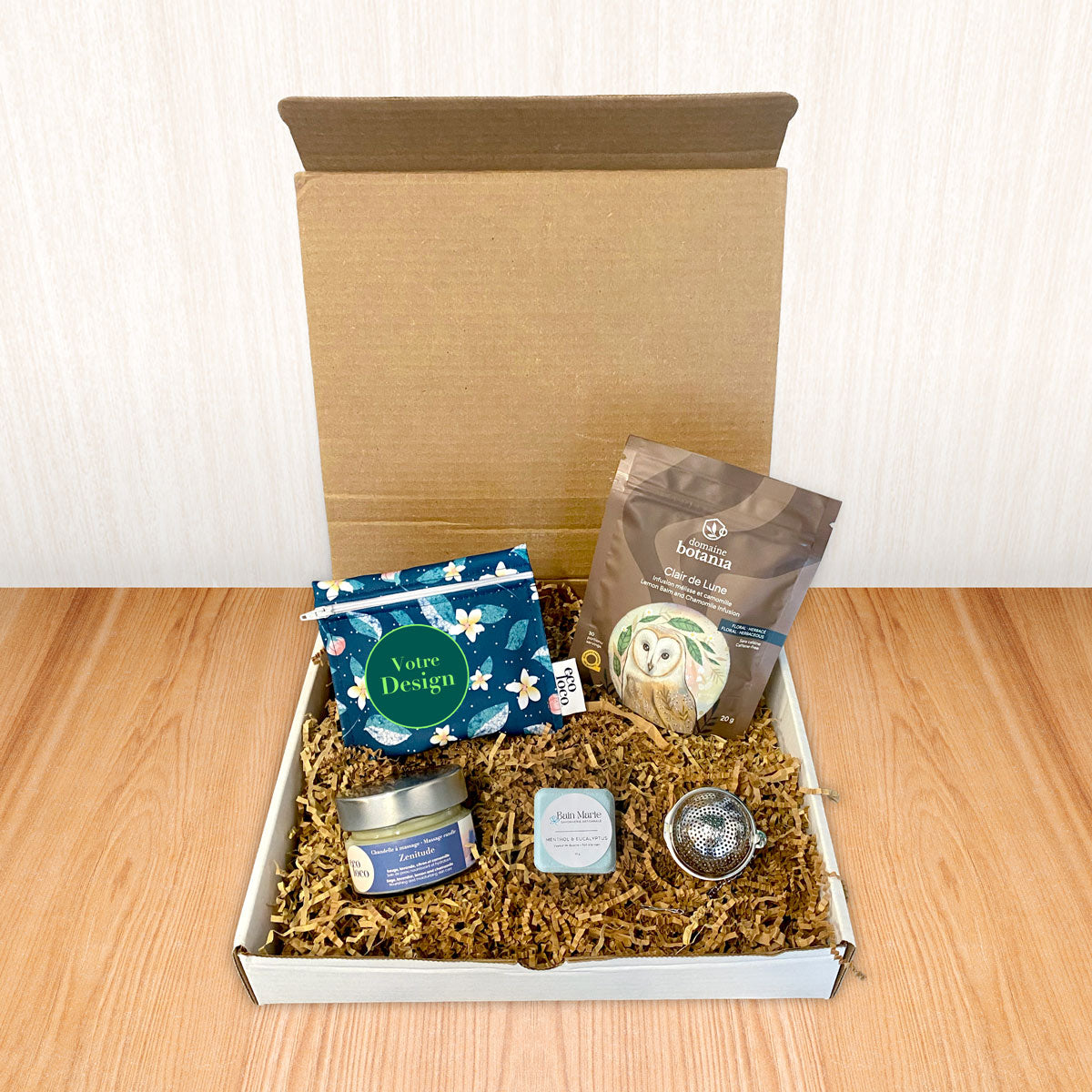 Une boîte cadeau écoresponsable avec à l'intérieur un sachet de tisane Claire de Lune illustration de hibou chouette, un petit sac à collation lavable, une chandelle à massage, une bombe de douche et une boule à thé