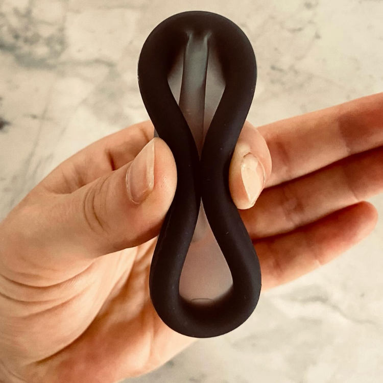 Un anneau de silicone représentant un disque menstruel écrasé par une main de femme sur un fond blanc marbré.