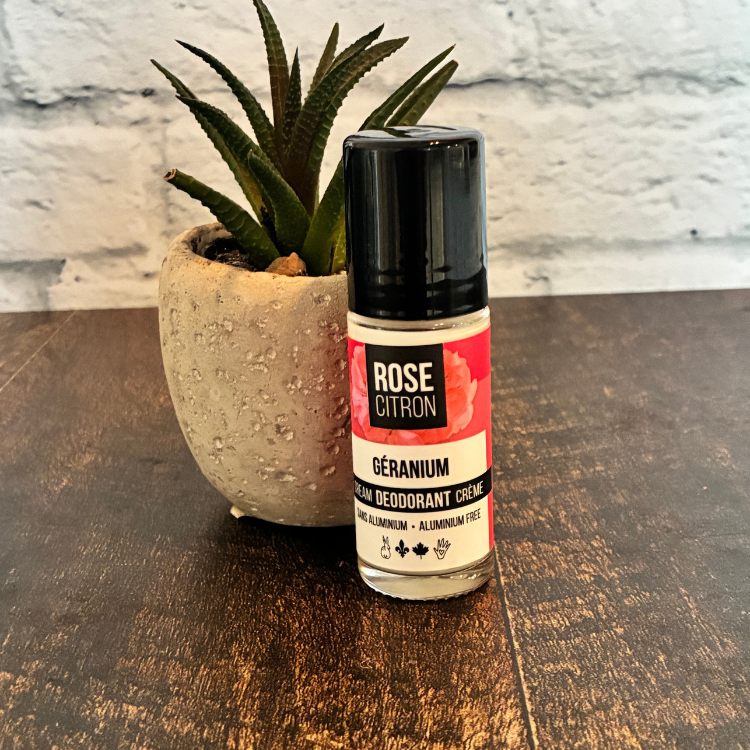 Bouteille de déodorant de la marque Rose Citron au géranium adossé à une petite plante avec une étiquette rouge pour l'odeur de géranium.