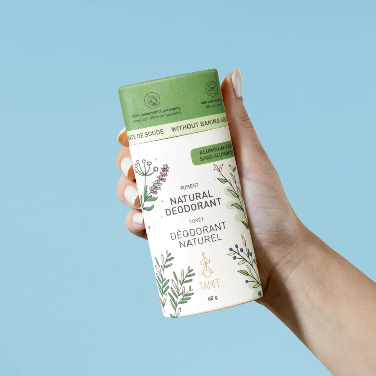 un tube de déodorant blanc et vert tenu dans une main de femme. On peut y lire déodorant naturel, sans bicarbonate et sans aluminium tanit Foret sur un fond bleu.