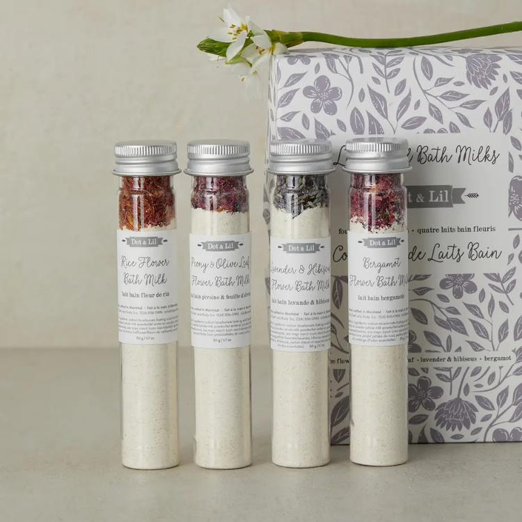 4 fioles au bouchon argenté comprenant 4 lait de bain différents de la marque Doc and Lil devait un coffret cadeau blanc avec des fleurs mauves et une petites fleures blanche sur le dessus.