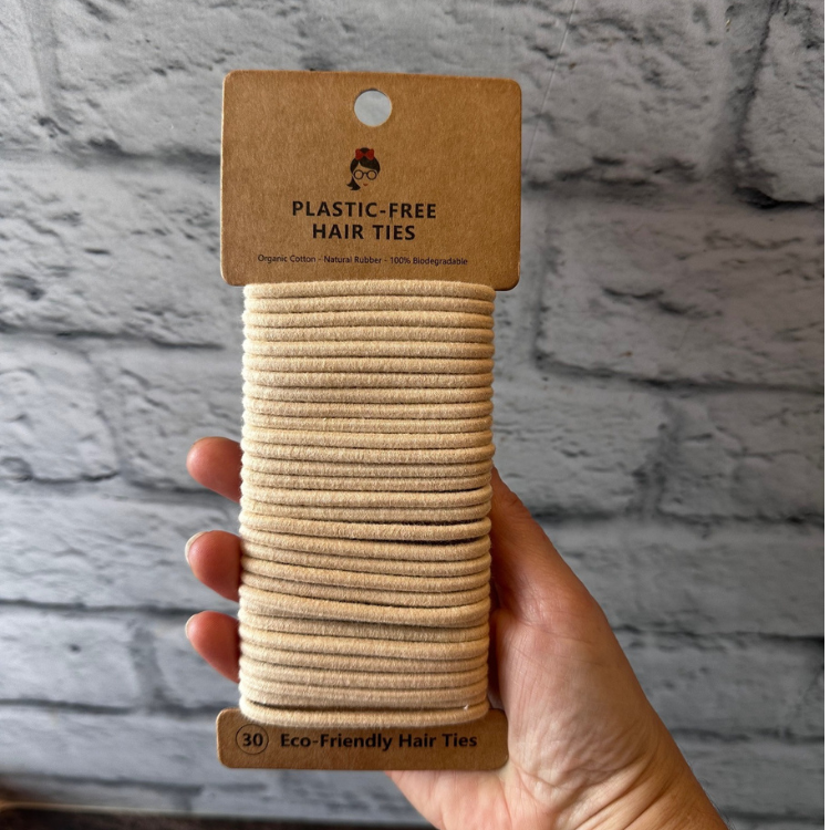 Paquet de 30 élastiques à cheveux sans plastique en silicone naturel de couleur crème tenu dans une main avec un fond de brique