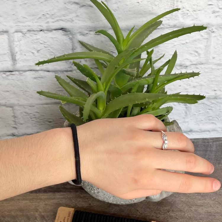 1 élastiquesà cheveux sans plastique en silicone naturel de couleur noir sur un poignet et avec en fond une plante et de la brique