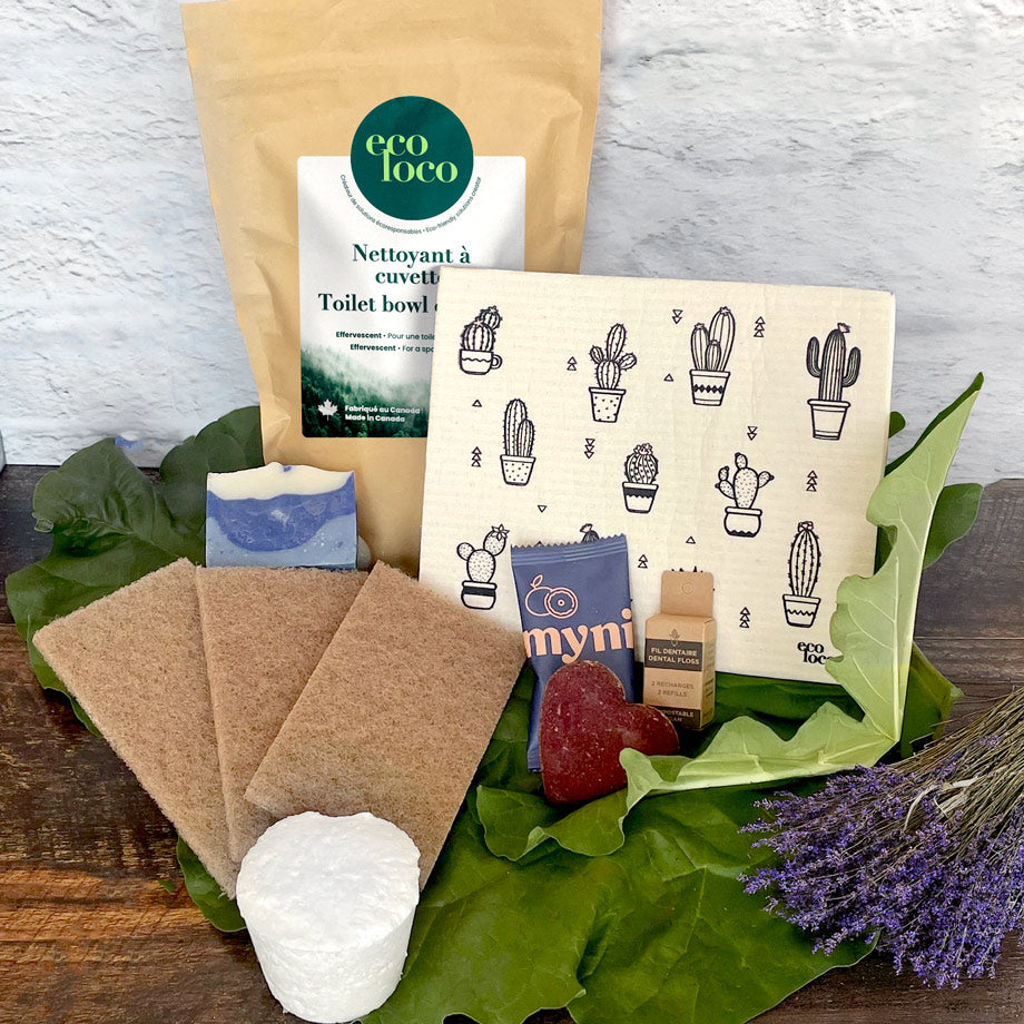 Ensemble de produits écoresponsable Nettoyant à cuvette avec un chiffon suédois, des éponges à récurer brunes, un cake vaisselle, un shampoing solide en forme de coeur, de la soie dentaire compostable sur un fond de feuilles vertes, de lavandes et un mur de briques blanches