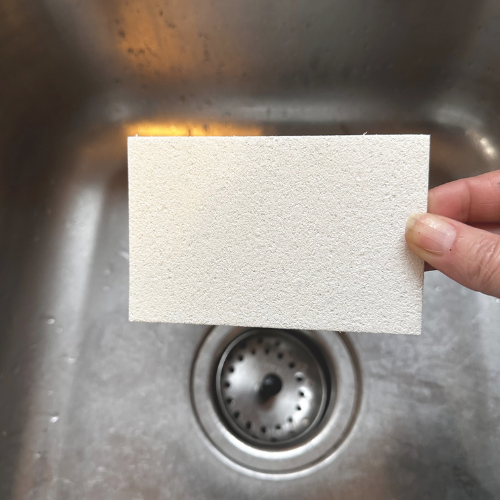 Éponge en cellulose ou pulpe de bois tenu dans une main au-dessus d'un lavabo.