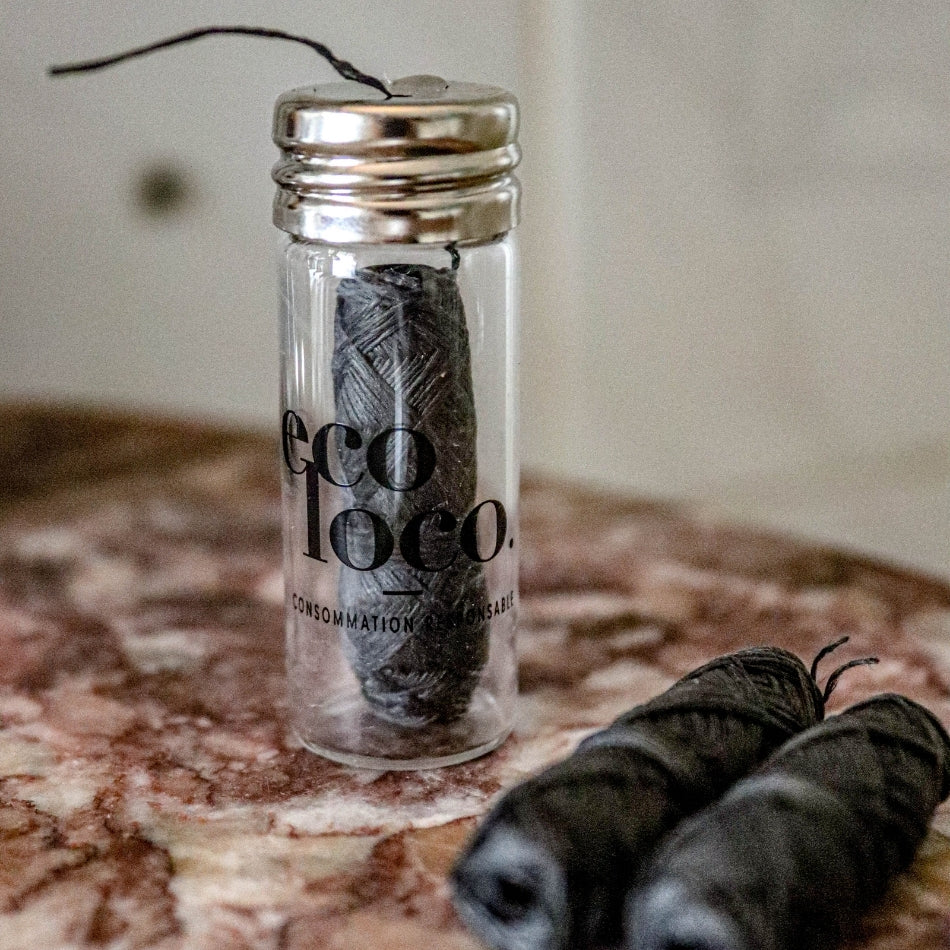 Fil dentaire noir de la marque Eco Loco dans un petit contenant en vitre transparent avec deux bobines de recharges sur un comptoir de granite brun