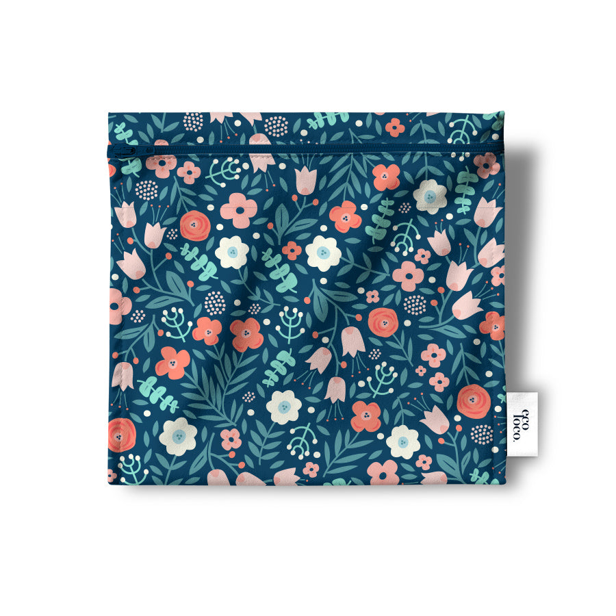 Un sac réutilisable en tissu pour les collations, sandwich, noix, biscuits, crudités, de couleur bleu avec des dessins petites fleures roses, blanches et orangée ainsi que des feuilles vertes. Le sac est à plat sur un fond blanc et porte l'étiquette de Eco Loco