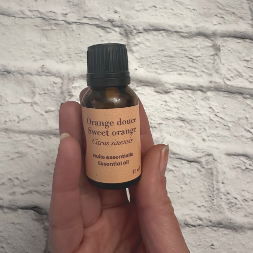 Flacon d'huile essentiel d'orange douce au dessus d'une brique blanche et tenue dans une main