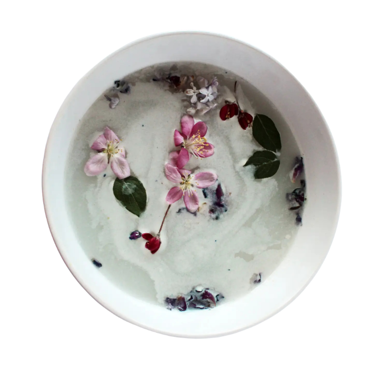 Un bol blanc avec un liquide laiteux et des fleurs sur un fond blanc.