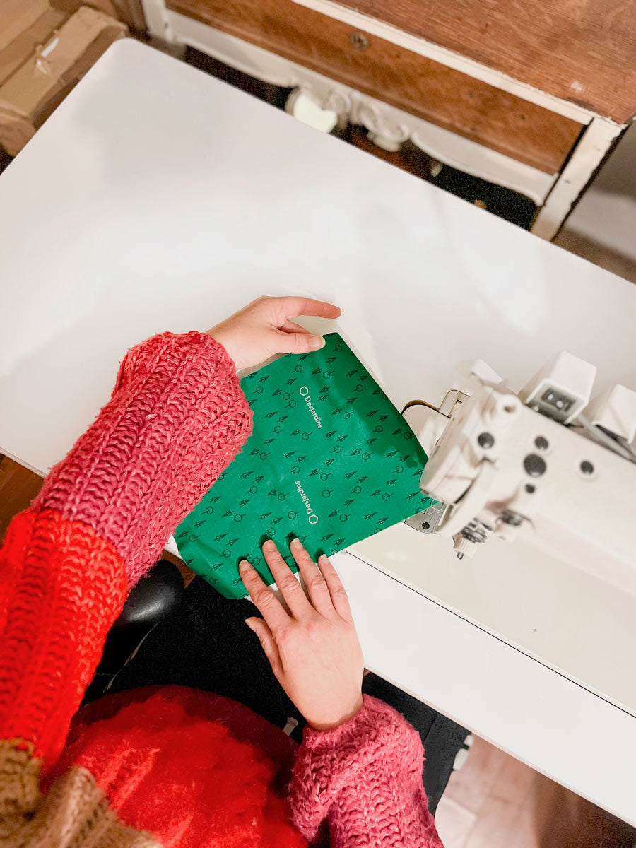 Une personne qui tient un morceaux de textile pour coudre un sac promotionnels écolo vert Desjardins machine a coudre chandail rouge