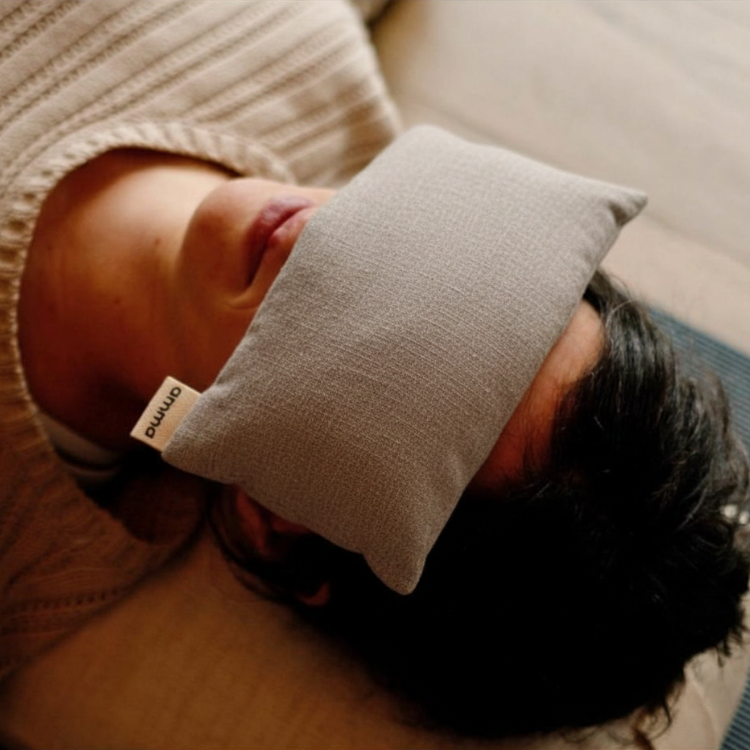 Le haut du corps d'une femme au cheveux courts couchée sur le dos avec un masque de relaxation sur les yeux de la marque Amma