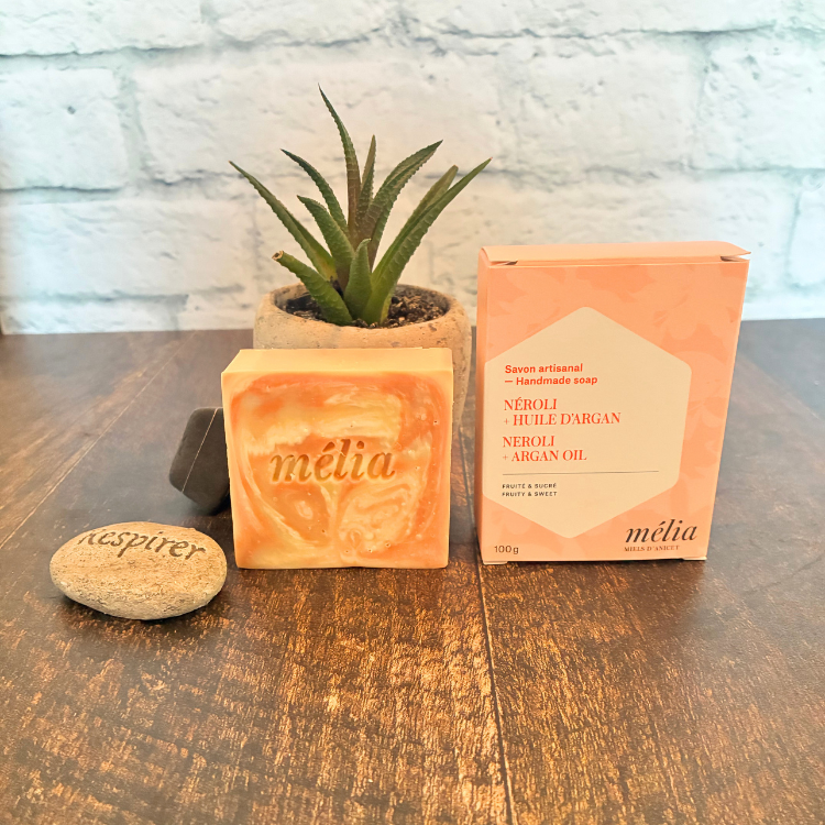 Le savon Néroli et huile d'argan et sa boite déposé sur une planche de boite avec une plante et une roche inscrite respirer.