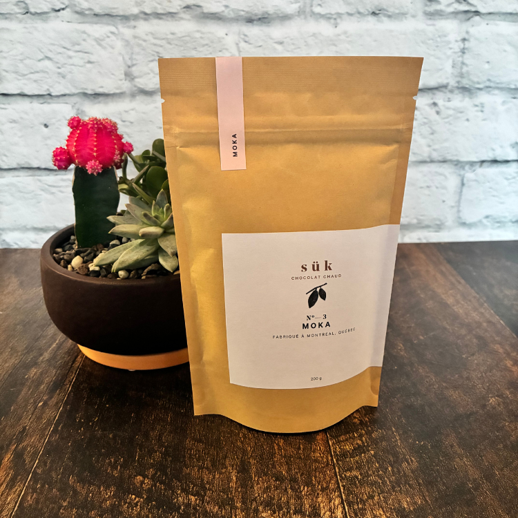 Sac de chocolat chaud Moka de SÜK une entreprise québécoise sur une planche de bois avec un mur de brique en arrière plan.