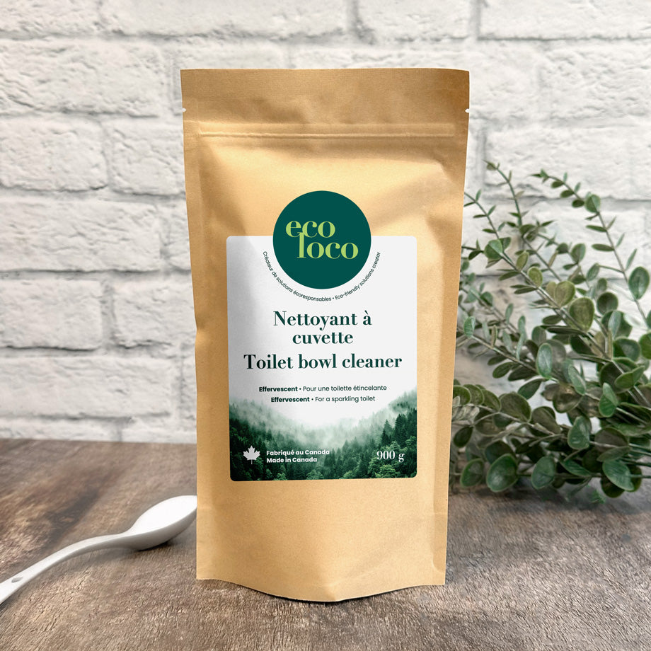 Pochette en papier kraft Eco Loco de nettoyant à cuvette toilette sur un fond de mur de briques blanches avec des feuilles vertes et une cuillère blanche