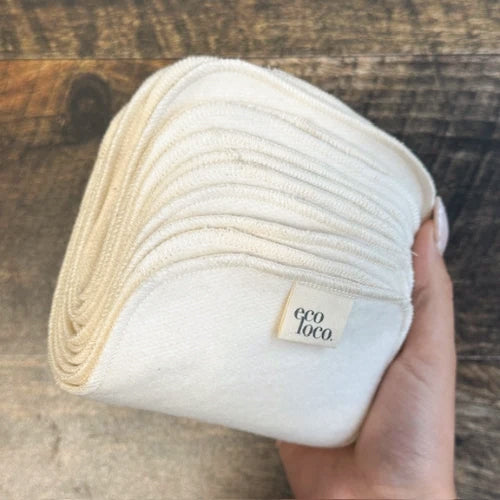 Une main qui tient du papier de toilette rectangulaire lavable beige en coton biologique avec une étiquette Eco Loco sur un fond de couleur bois foncé