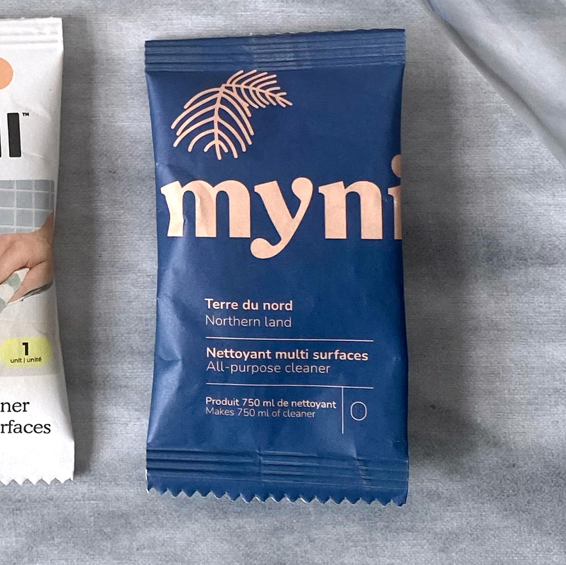 Petit sachet bleu foncéécrit Myni Terre du Nord nettoyant multi surfaces sur un fond de textile gris