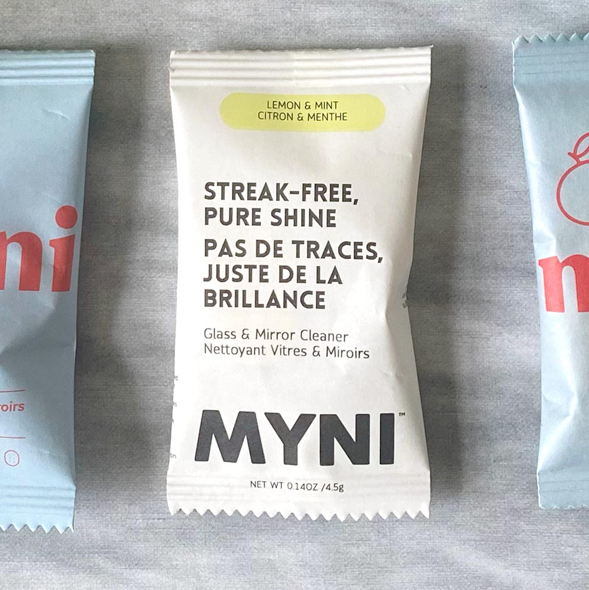 Petit sachet blanc écrit Myni Citron & menthe nettoyant vitres & miroirs sur un fond de textile gris