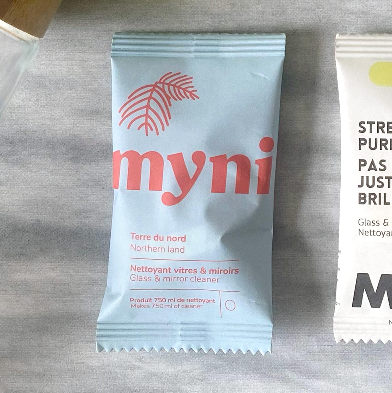 Petit sachet bleu pâle écrit Myni Terre du Nord nettoyant vitres & miroirs sur un fond de textile gris
