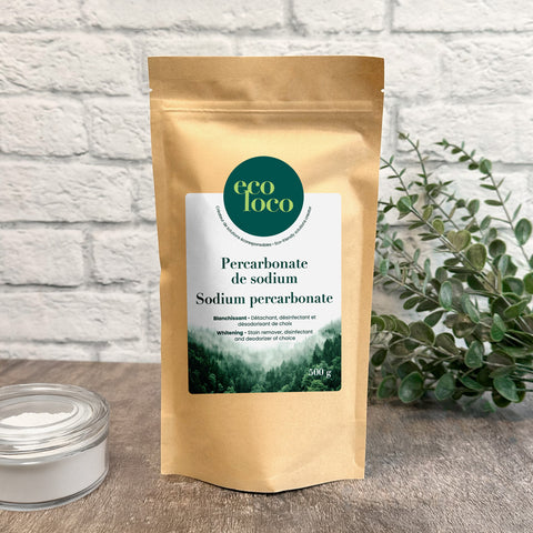 Pochette en papier kraft Eco Loco de Percarbonate de Sodium soude sur un fond de mur de briques blanches avec des feuilles vertes et un petit bol en vitre verre contenant de la poudre blanche
