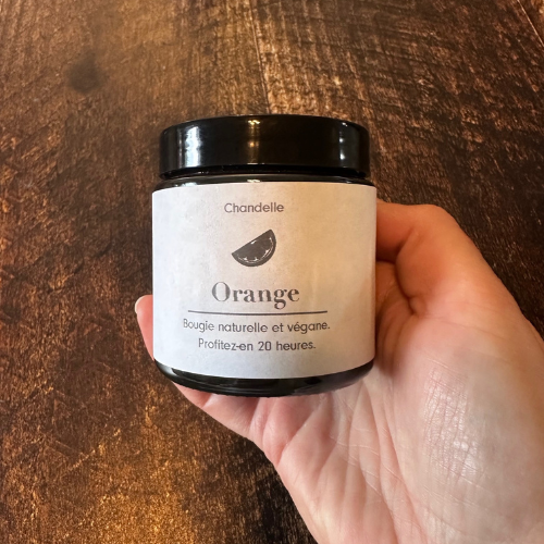 Bougie orange tenue dans une main sur un planche de bois