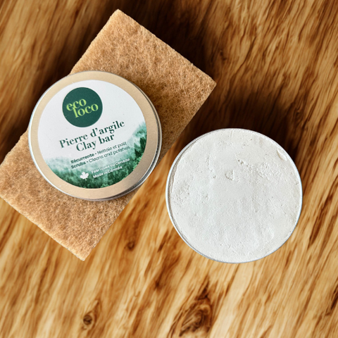 Boîte métallique de pierre d’argile Eco Loco, ouverte en deux, nettoyante et polissante, posée sur un comptoir de cuisine en bois avec une éponge naturelle brune.