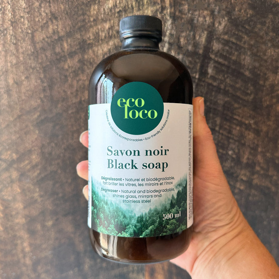 Bouteille de savon noir black soap tenue par une main et un fond en bois