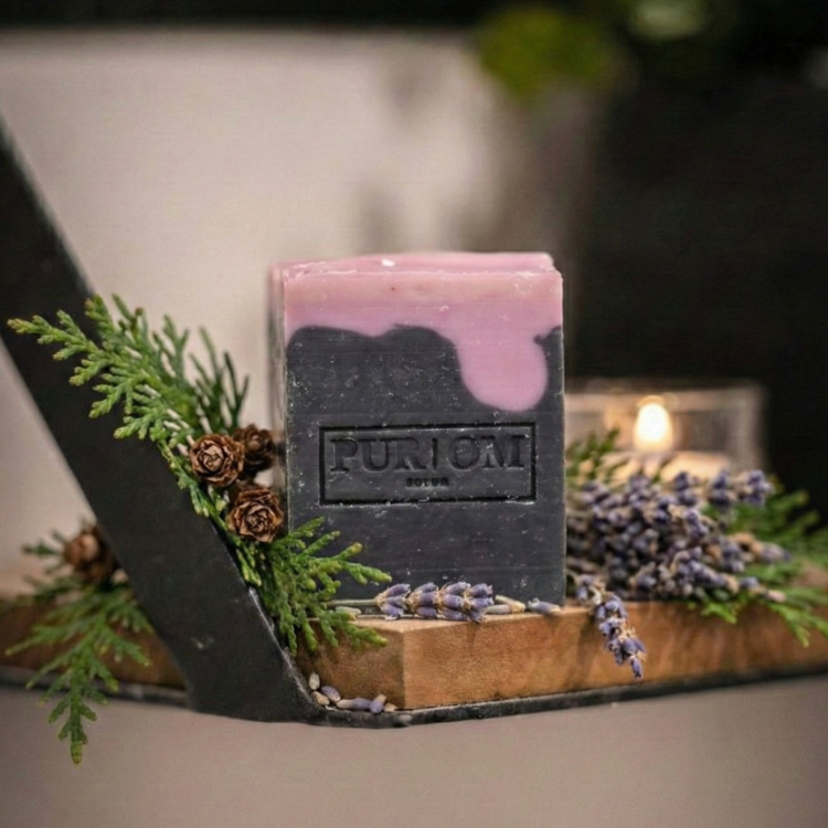 Savon l'autentique de pur om avec des feuilles de sapin et des fleurs de lavande ainsi qu'une chandelle en arrière plan.