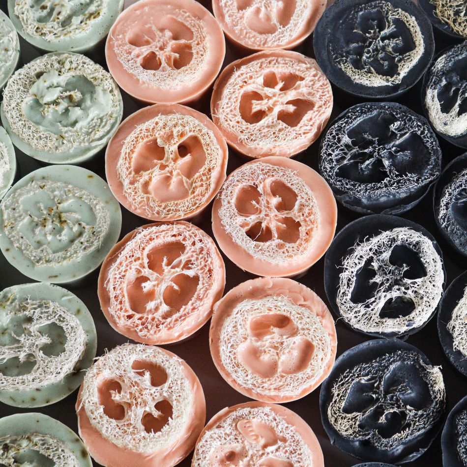 Plusieurs savons avec une luffa à l'intérieur de couleur vert, rose pêche et noirs