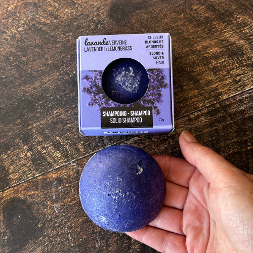 Shampoing en barre pour cheveux blonds et blancs tenu dans une main et déposé sur un plache de bois.