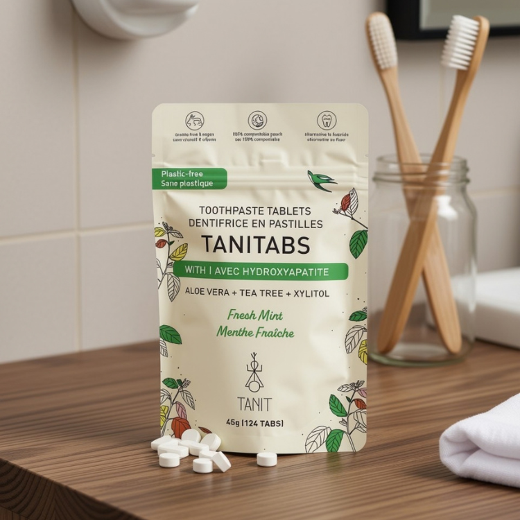 Un sachet de dentifrice en pastilles sur lequel il est écrit Tanitab menthe fraiche Tanit 124 tabs déposé sur un comptoir de salle de bain avec un porte savon et deux brosses à dents en bambou dans un pot Mason.