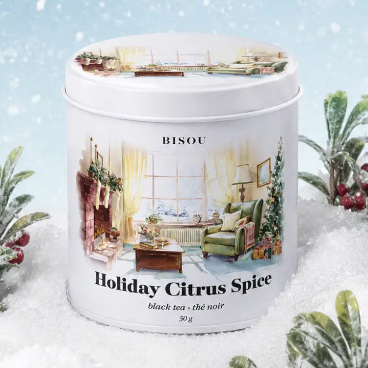 Une boite ronde et blanche avec un dessin d'un salon chaleureux comprenant une chaise verte et un foyer et des inscription Bisou Holiday Citrus Spice entouré de neige et de plantes.