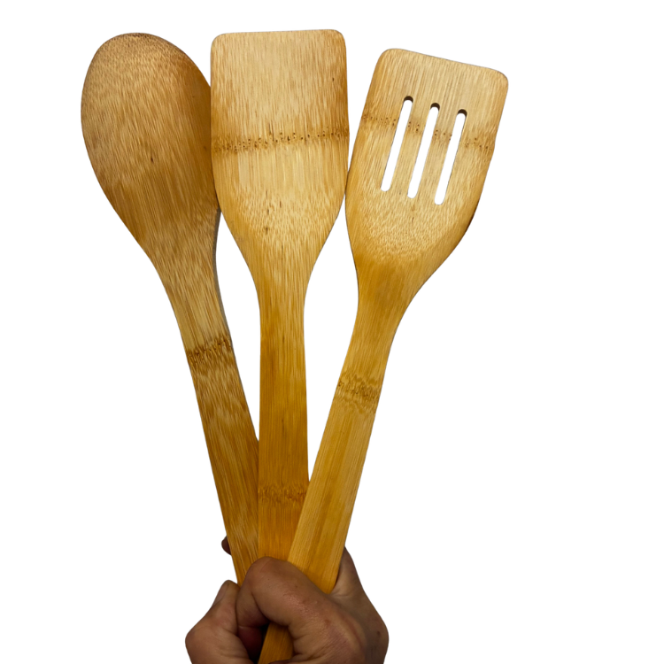 3 grands ustensiles de cuisines en bois tenu dans une main sur un fond blanc.