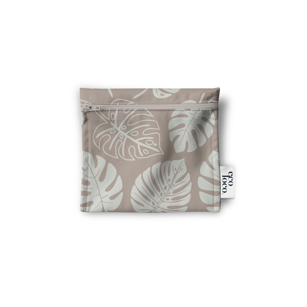 Un sac réutilisable en tissu pour les collations, noix, biscuits, crudités, de couleur beige avec des feuilles tropicales de couleur blanche. Le sac est à plat sur un fond blanc.