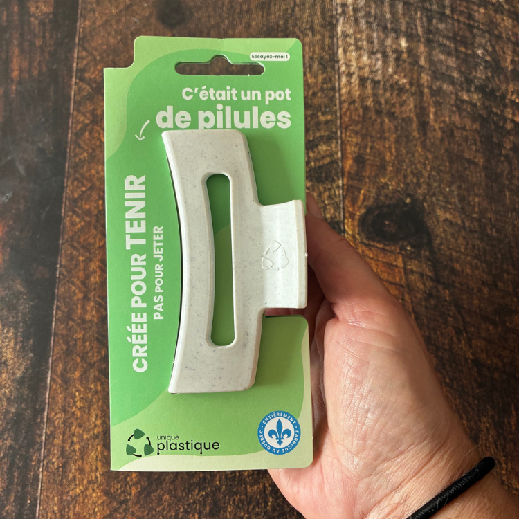 Pince à cheveux blanche avec un logo de matériau recyclé et son emballage cartonné vert qui dit: C'était un pot de pilules, créée pour tenir pas pour jeter, Unique plastique et le logo fait au Québec.