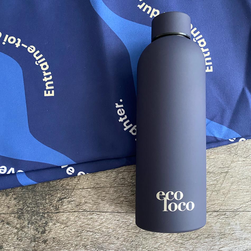 Bouteille d'eau mauve profond violet viollette en acier inoxydable sur un fond de bois et une serviette de sport en microfibre