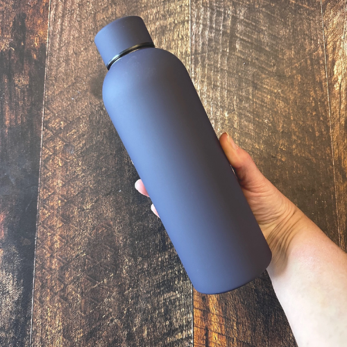 Une bouteille d'eau réutilisable en acier inoxydable de couleur violet nuit au dessus d'une planche en bois.