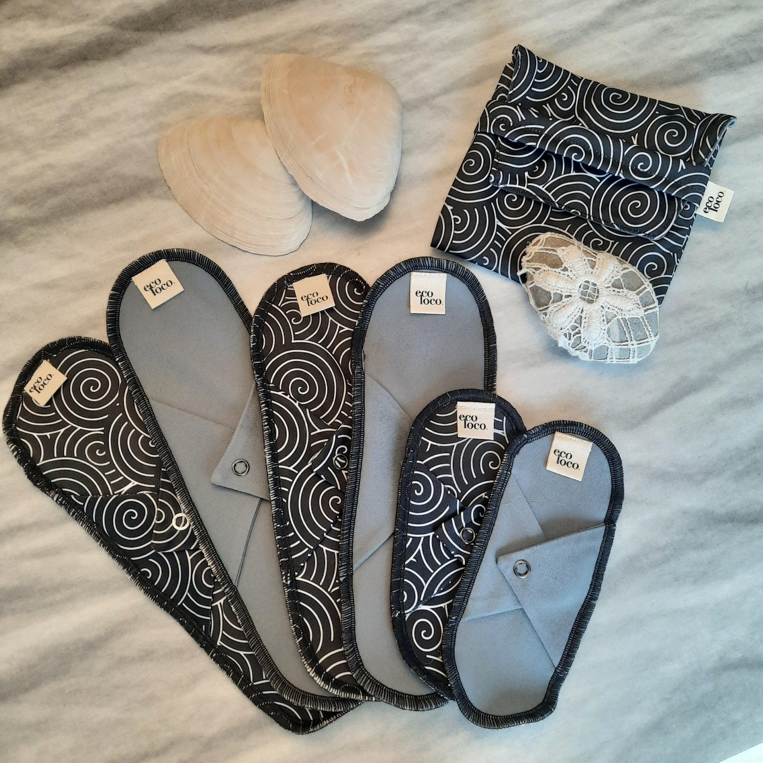 Grand ensemble de serviettes hygiéniques lavables faites de coton biologique et de tissu imperméable en bouteille de plastique recyclé avec des motifs noirs et blancs.