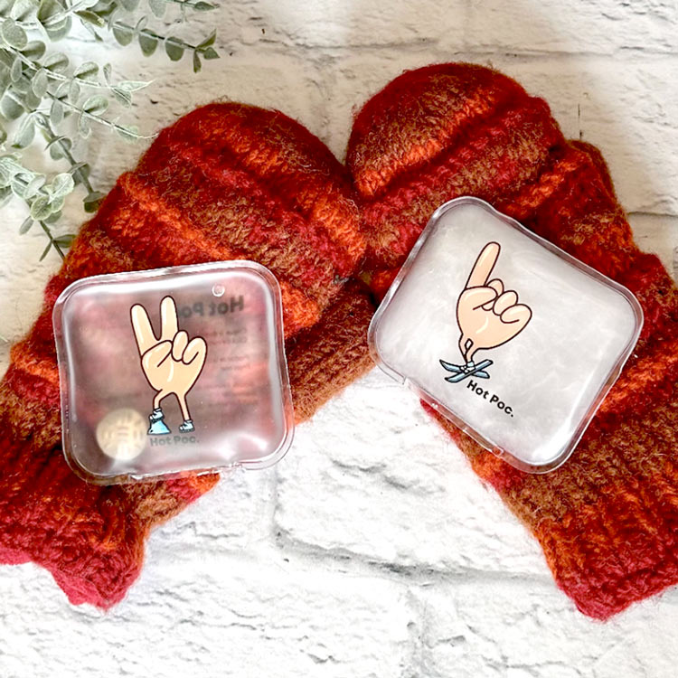 Deux mitaines rouges avec des pastilles Hot poc dessus sur une fond texture de briques blanches et feuillage vert