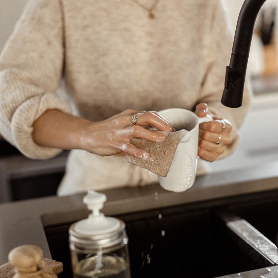 Mains de femme qui lave une tasse avec des produits savonneux écologiques et écoresponsables dans une cuisine