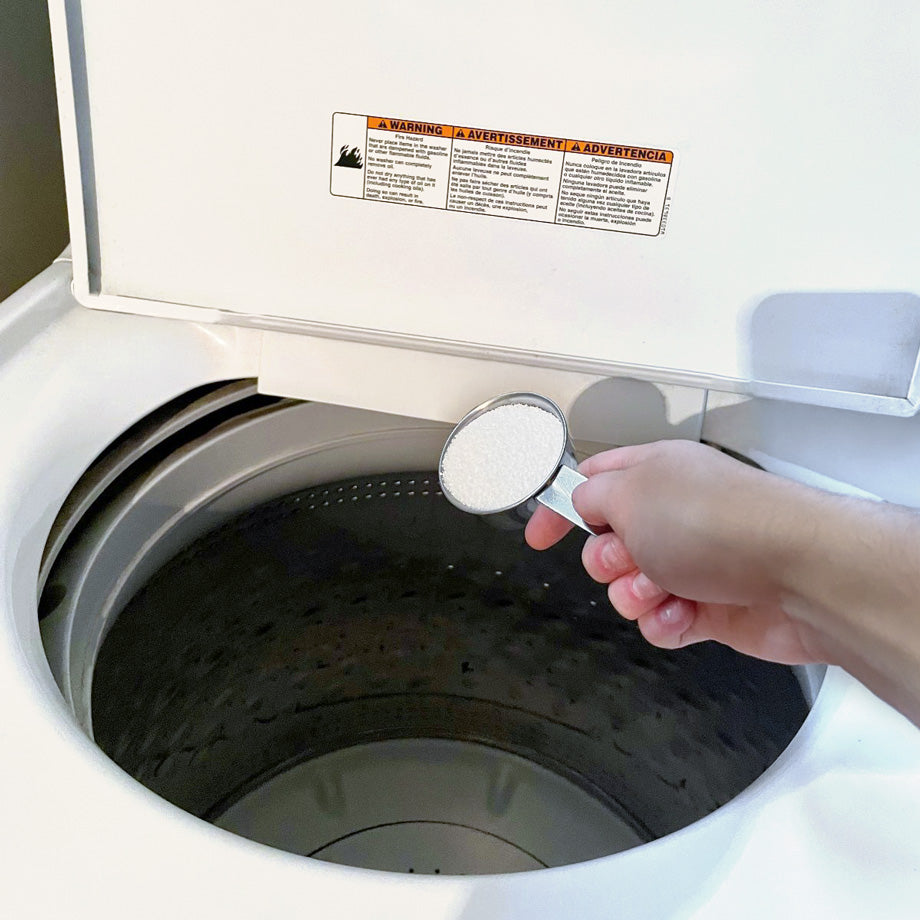 Une main qui déverse de la poudre blanche dans une laveuse à linge