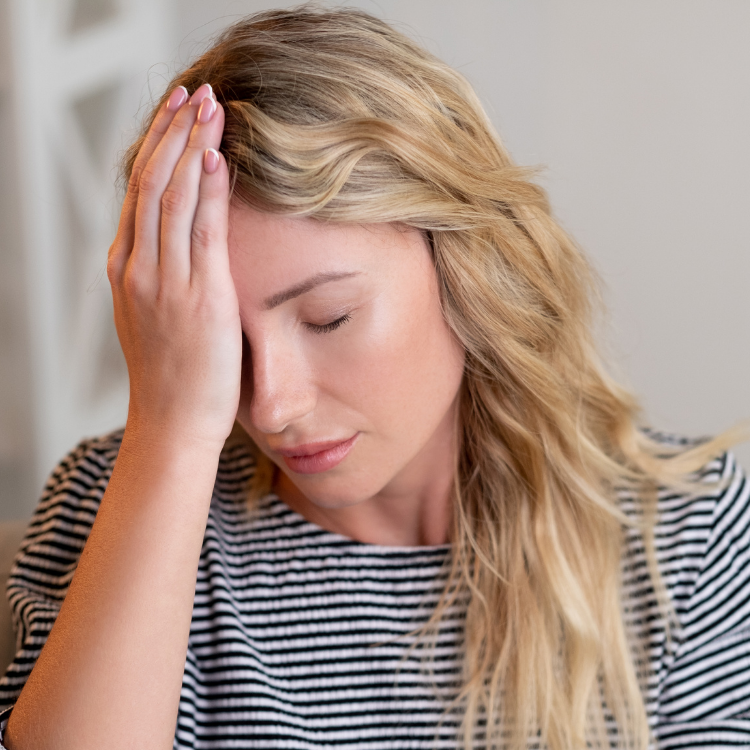 Femme au cheveux blonds avec un chandail rayé se tenant la tête d'une main.