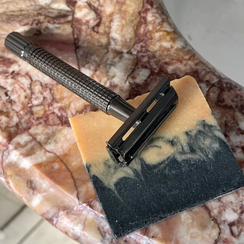 Rasoir de sûreté noir apposé sur un savon noir et orange et un lavabo en marbre