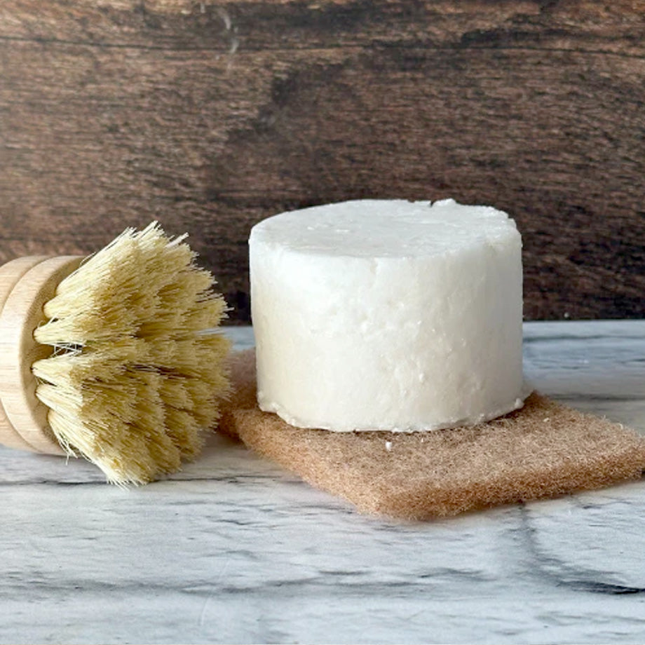 Recharge de cake vaisselle fait par Eco Loco sur une éponge brune en coquille de noix écoresponsable avec une brosse en bois sur un comptoir blanc et un fond de mur en bois foncé