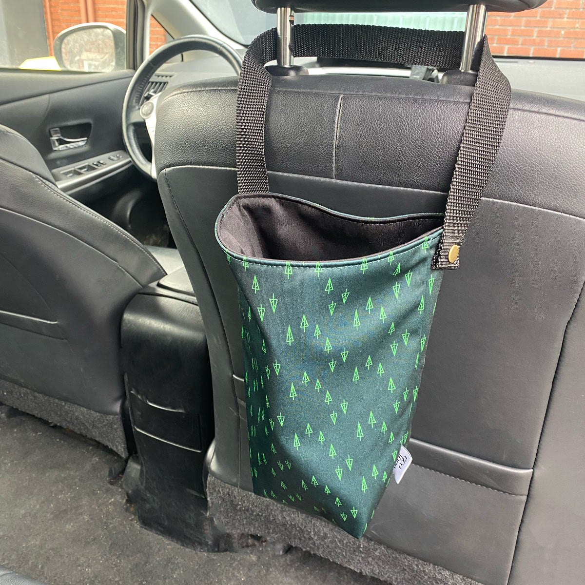 Corbeille poubelle de voiture accrochée sur un banc de cuir noir avec un motif de petites sapins verts