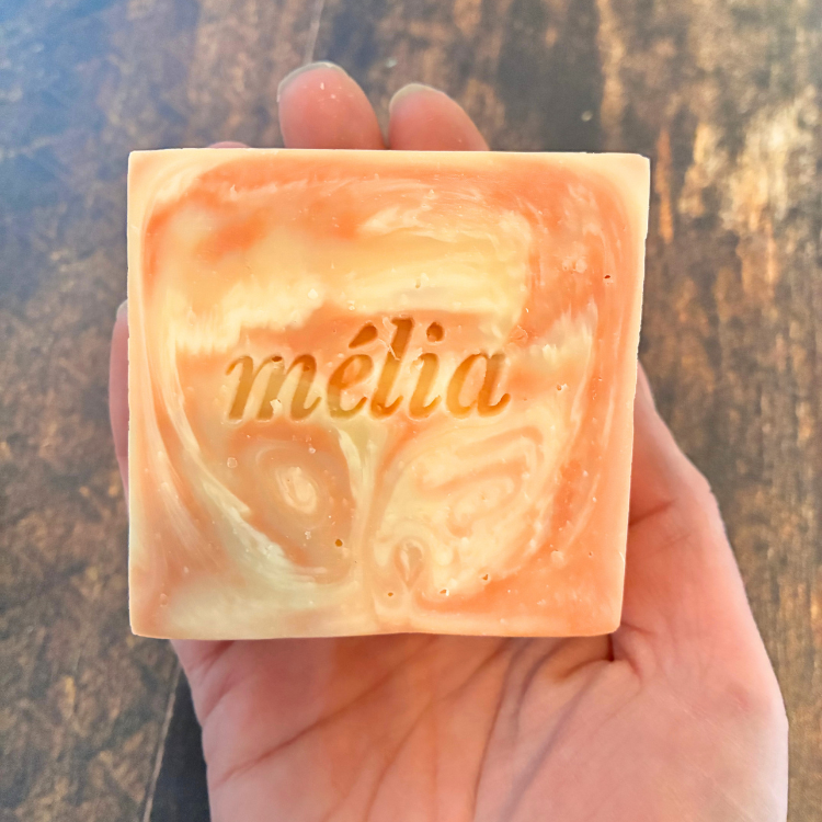 Le savon de la marque Mélia au néroli et à l'huile d'argan tenu dans une main au dessus d'une planche.