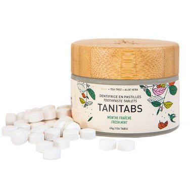 Un pot de dentifrice en pastilles sur lequel il est écrit Tanitab menthe fraiche avec plusieurs pastilles sorties du pot sur un fond blanc.
