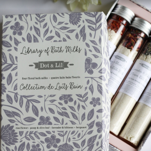 4 fioles au bouchon argenté comprenant 4 lait de bain différents de la marque Doc and Lil devait un coffret cadeau blanc avec des fleurs mauves et une petites fleures blanche sur le dessus.