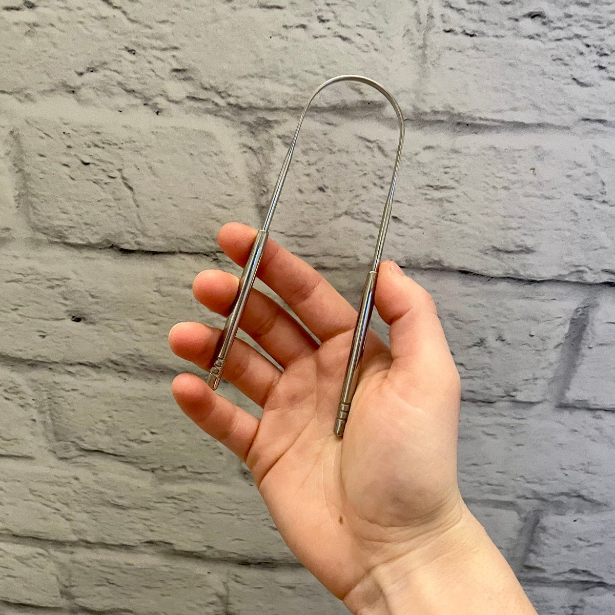 nettoie langue en acier inxydable tenu dans une main sur un fond de brique blanche